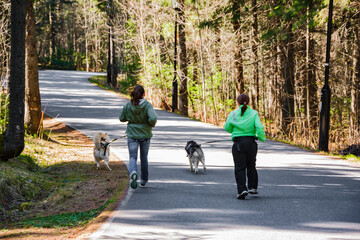 Two women in the woods with two dogs running on the road