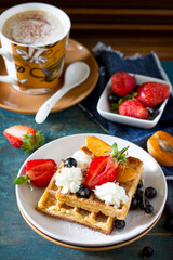 Delicious breakfast from a cup of coffee and waffles with strawberries on a vintage blue background.