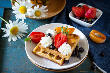 Delicious breakfast from a cup of coffee and waffles with strawberries on a vintage blue background.