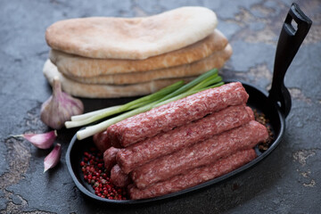 Frying pan with raw cevapi or cevapcici sausages and pitas, selective focus, studio shot