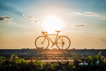 Silhouette of bicycle on the road in front of sunset background.