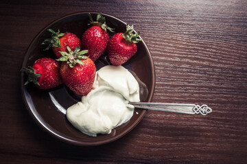 Strawberries with a spoon of cream on a plate