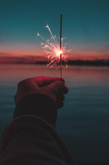 a hand holding a sparkler in the sunset