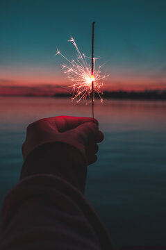 a hand holding a sparkler in the sunset