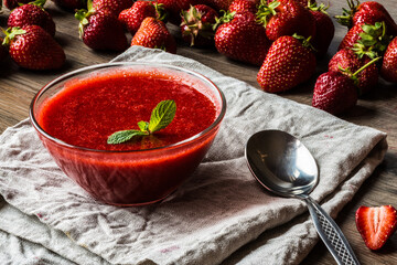 A bowl of strawberry sauce with a spoon on a linen tissue napkin