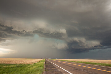 A powerful supercell thunderstorm looms over a highway on the plains.