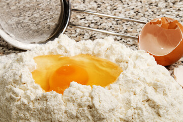 freshly opened egg in flour and sieve in the background