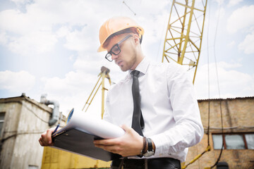 Engineer builder in a helmet holds drawings at construction site