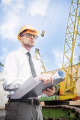 Engineer builder in a helmet holds drawings at construction site