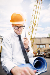 Engineer builder in a helmet holds drawings at construction site