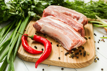 Raw pork ribs with vegetables and pepper on a cutting board.