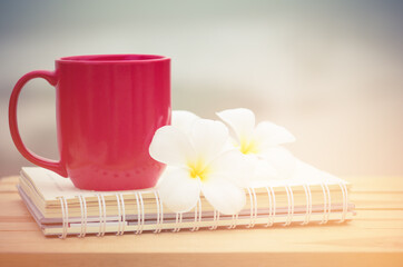red coffee cup with notebook and white flower on wood table