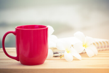 red coffee cup with notebook and white flower on wood table