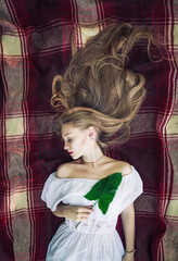 Young, beautiful blonde woman lying in bed on red coverlet. Closed eyes