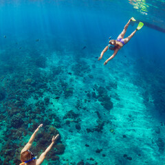 Happy family - couple in snorkeling masks dive deep underwater with tropical fishes in coral reef...