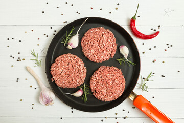 Organic beef raw cutlets with spices in a frying pan on a white background with garlic, rosemary...