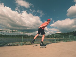 Rear view to inline skater in red t-shirt and black pants skating on the bridge . Outdoor inline...