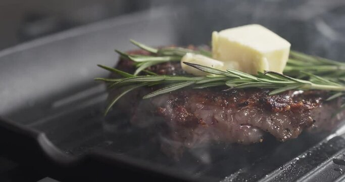 Slide slow motion shot of cooking rib eye steak with herbs and butter on top on grill pan, 4k 60fps prores footage