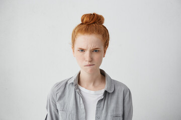 Portrait of angry frowning teenager having ginger bun biting her lip with anger isolated over white background. Young freckled redhead woman having dissatisfied expression after hearing bad news