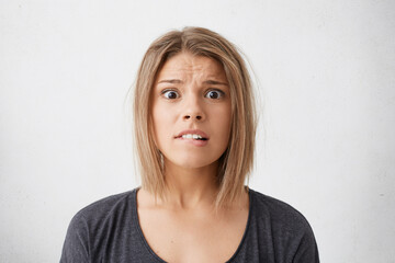 Scared beautiful Caucasian young female biting her lower lip having nervous expression and wide opened eyes worrying about important event in her life posing in studio over white background.