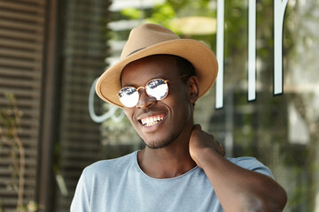 Portrait of smiling stylish dark-skinned man wearing casual T-shirt, summer hat and round...