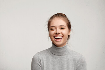 Headshot of good-looking lucky woman with tied hair pure skin and broad smile being happy to watch at camera. Sincere female with beautiful appearance wearing casual clothes isolated over white wall - obrazy, fototapety, plakaty