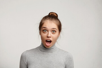 Astonished young beautiful fair-haired woman looking at camera with wide opened mouth and eyes being surprised to hear horror news. Emotional woman staring at camera with jaw dropped posing in studio