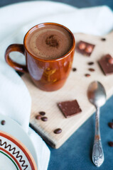Ceramic brown mug of milk coffee on wooden board with coffee beans and chocolate.