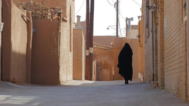 Muslim woman in traditional chador walking on street in Old city of Yazd, Iran