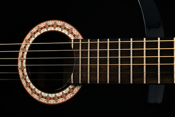 A black Six-string classical acoustic guitar isolated on black background.