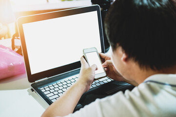 a guy working using computer laptop, and smart phone with blank white screen