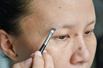  asian woman applying makeup with eyebrow brush
