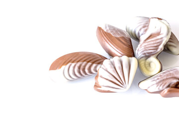 Chocolate candy in the form of sea shells on white table with reflection isolated on white background