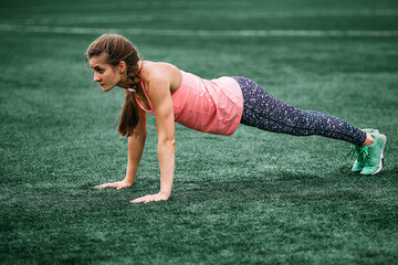 A beautiful muscular girl in tights and a vest makes a warm-up at the stadium. Cross fit, fitness,...