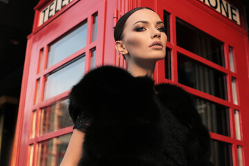 beautiful girl with dark hair walking by the street, red phone booth on background