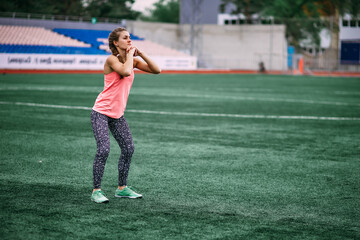 A beautiful muscular girl in tights and a vest makes a warm-up at the stadium. Cross fit, fitness, healthy lifestyle