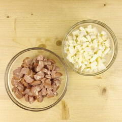Chopped wurstel and mozzarella in a transparent bowl on wooden background - top view