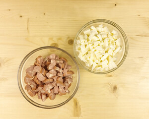 Chopped wurstel and mozzarella in a transparent bowl on wooden background - top view