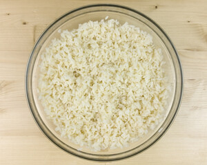 White rice in a transparent bowl on wooden background - top view