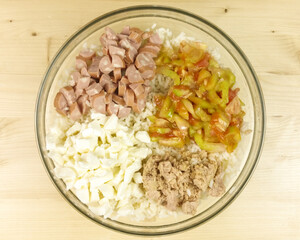 Making simple rice salad in a transparent bowl on wooden background - top view
