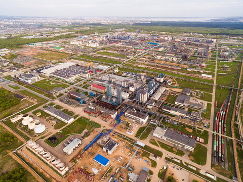 A huge oil refinery with pipes and distillation of the complex on a green field surrounded by forest. Aerial view