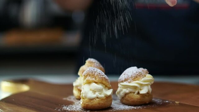 Pastry chef hand springkling, icing sugar power over cream puff in slow-motion 