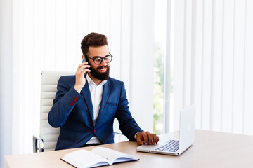 Obraz premium Businessman on his work place using laptop and phone to communicate with others