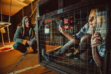 Bloody maniac and his female victim in the cage. - obrazy, fototapety, plakaty