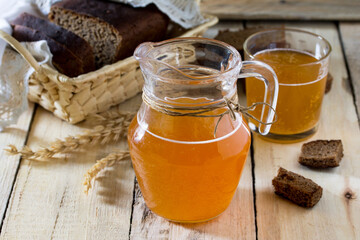 Traditional Russian cold rye drink Kvas in a glass and a jug on the kitchen table in a rustic...