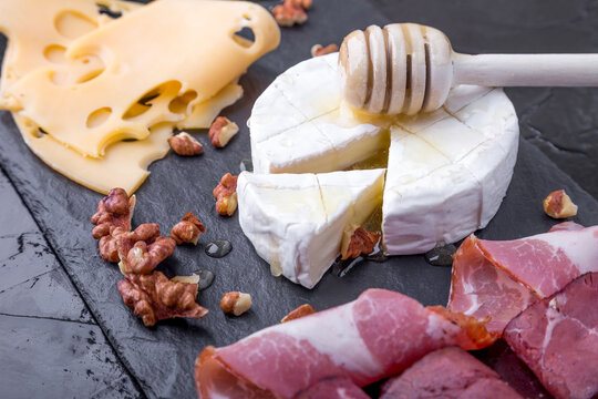 Cheese and meat plate with walnuts on black slate plate background. Camembert with honey