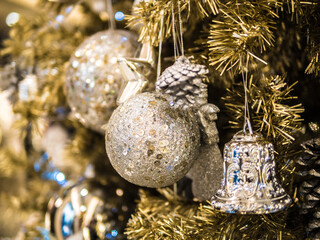 close up white bauble hanging and bell from a  Decorated Christmas tree, Christmas tree decoration,with various gold leaf, lighting decoration blurred is background