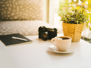 coffee cup, Retro camera, notebook, white pen and Plastic plants on white table in the coffeeshop the sun's rays in the morning