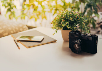 Retro camera, Modern smartphone, pen,  and black Notebook on white table with sunlight in the morning