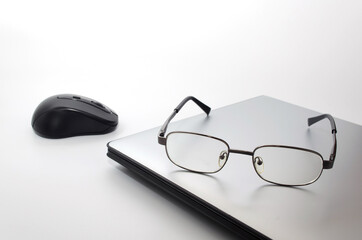 Laptop computer with wireless black mouse and eyeglasses isolate on white background, selective focus, copy space